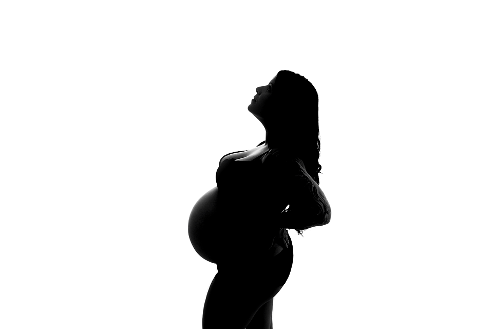 A silhouette of a pregnant woman stands in a studio with a hand on her back