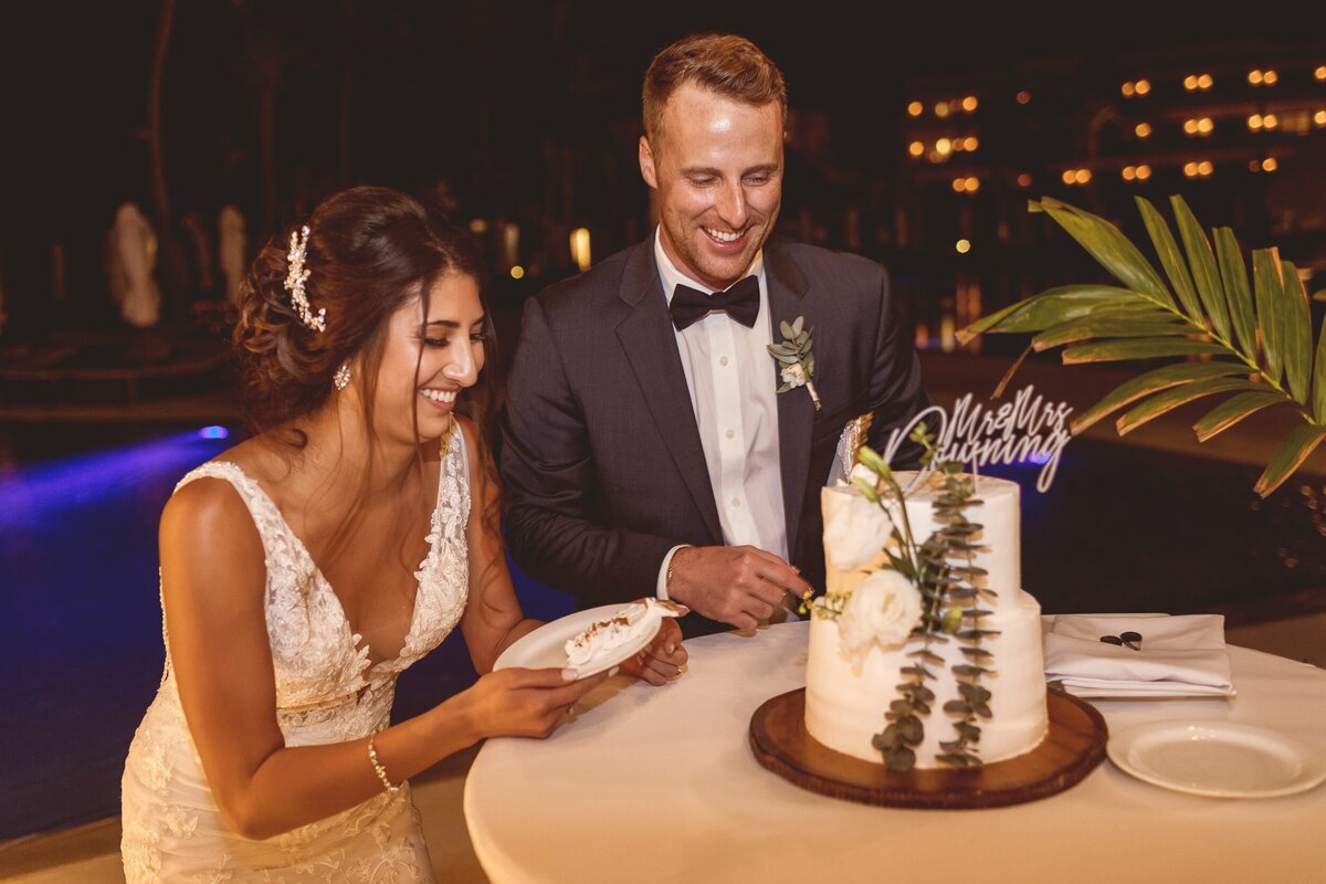 Bride and groom laughing and cutting cake at wedding in Riviera Maya