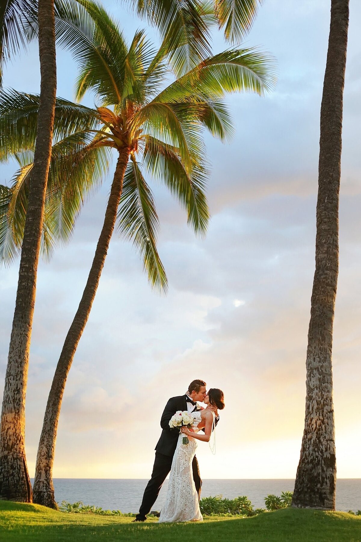 Bride and groom kiss between palm trees after Love + Water capture their wedding at the Andaz Maui