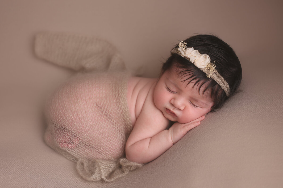 Baby sleeping curled up on her tummy and leaning on her hand on a beige background with a headband on.