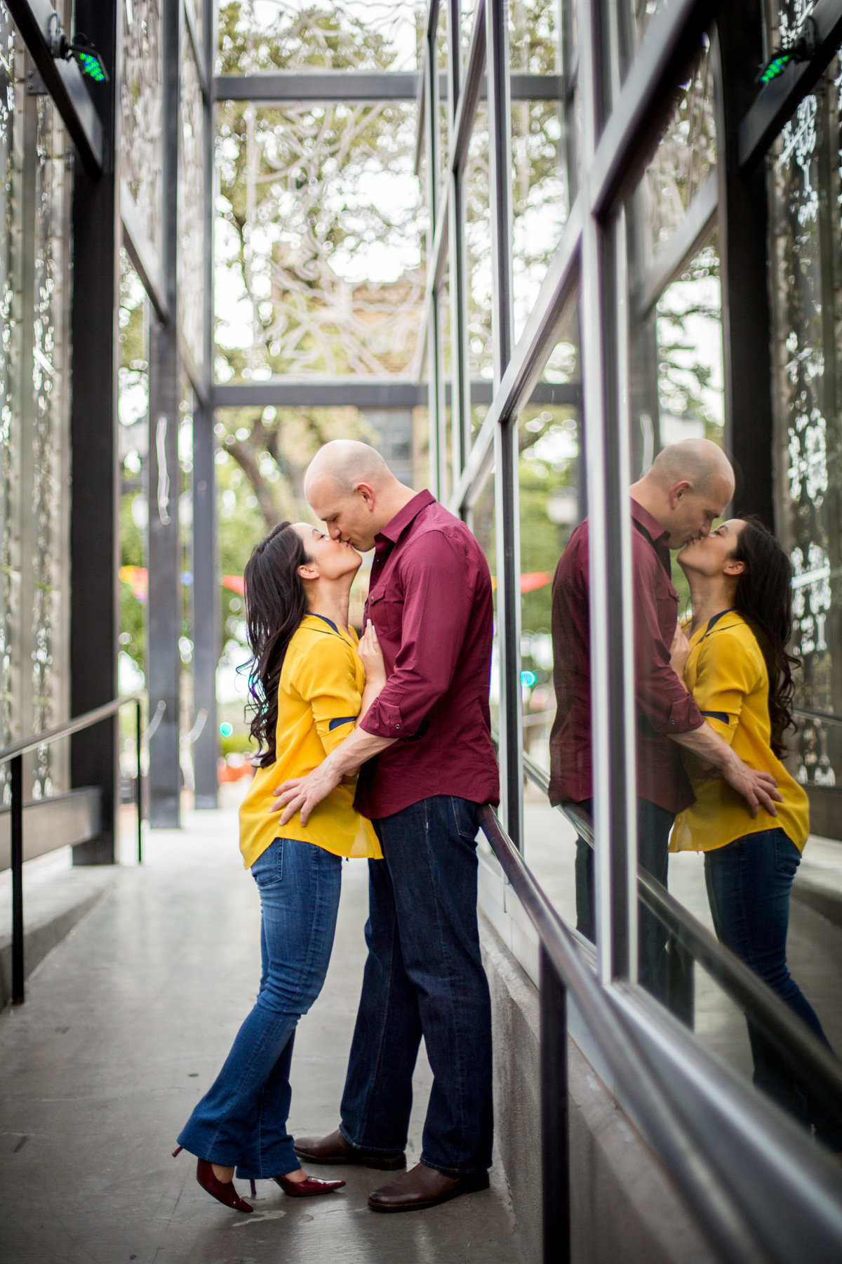 Engaged couple embracing and kissing and you can see their reflection on the building next to them.
