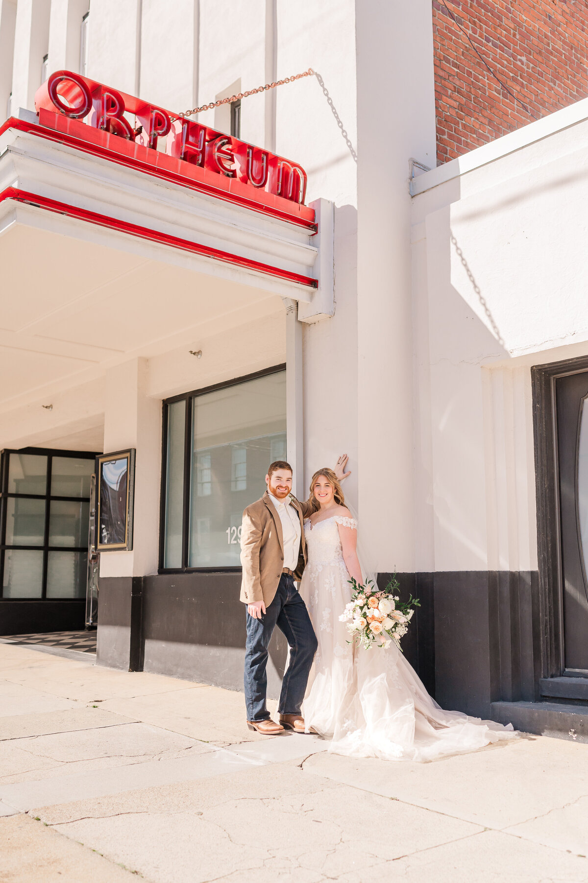 A newly married couple posing for portraits under the sign at The Orpheum after their wedding ceremony by Raleigh wedding photographer, JoLynn Photography