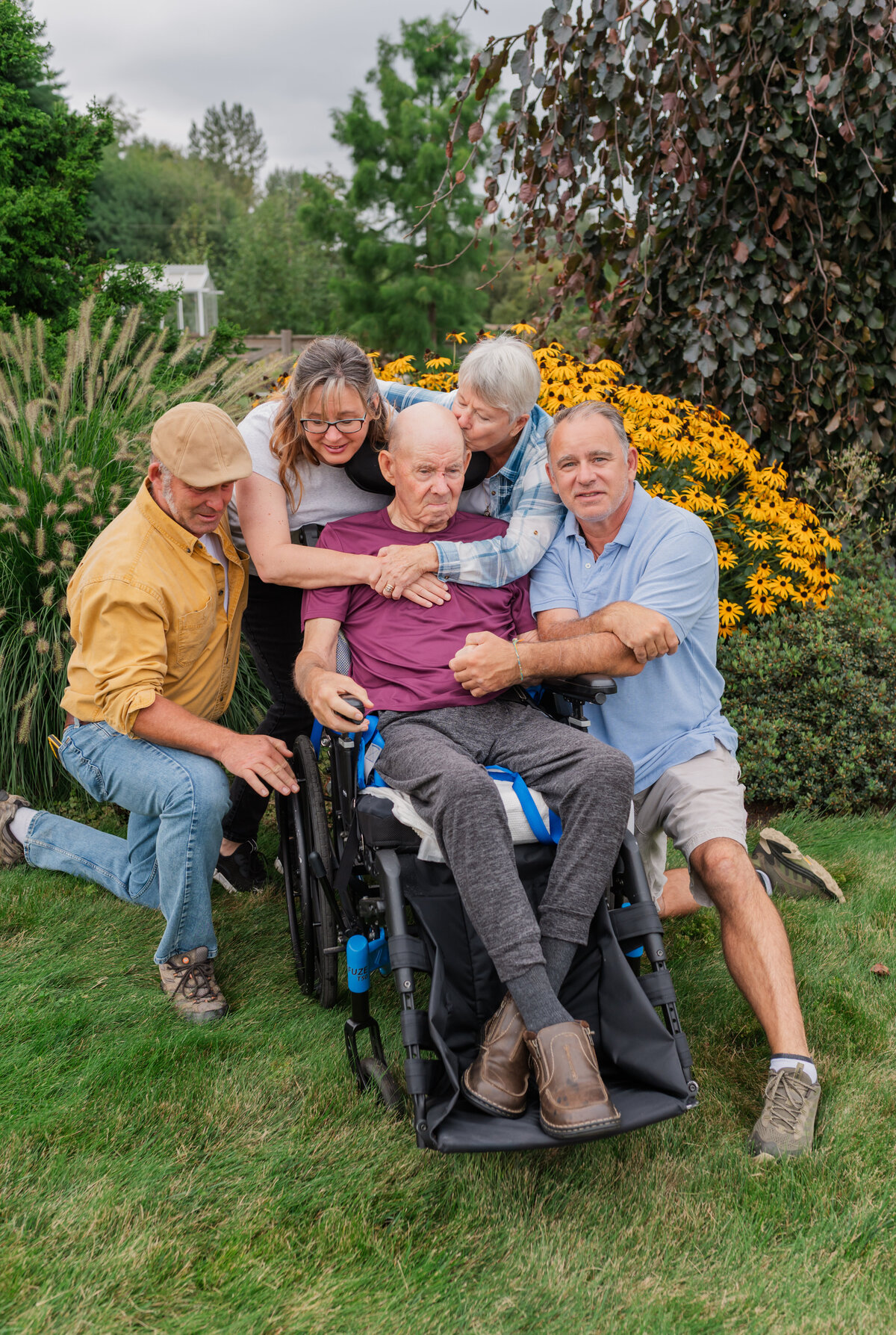 Dad sitting in a wheelchair, Kids hugging their dad and mom kissing dads forehead. 