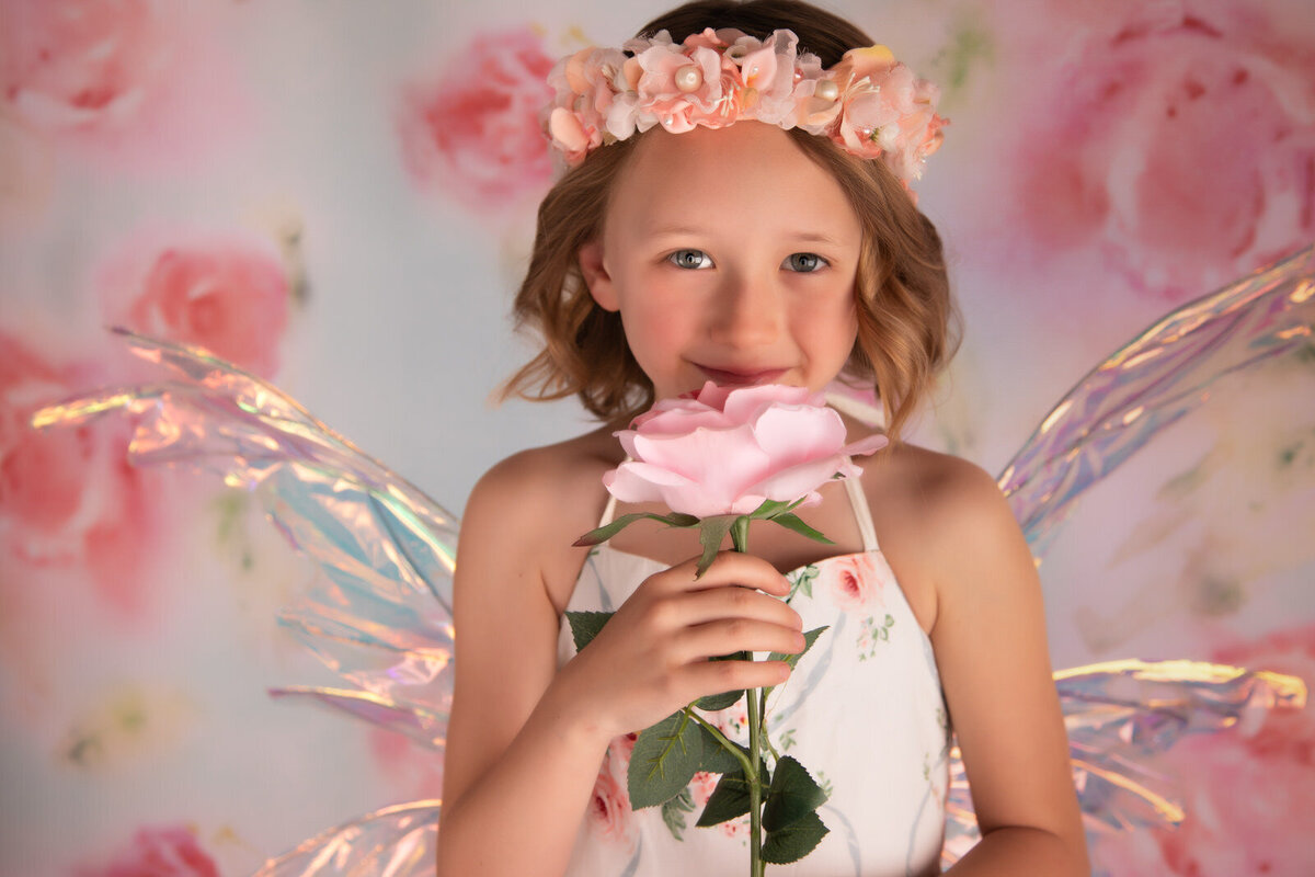 girl-holding-flower-in-studio-wearing-pink-floral-dress-against-a-pink-floral-background-arlington-tx