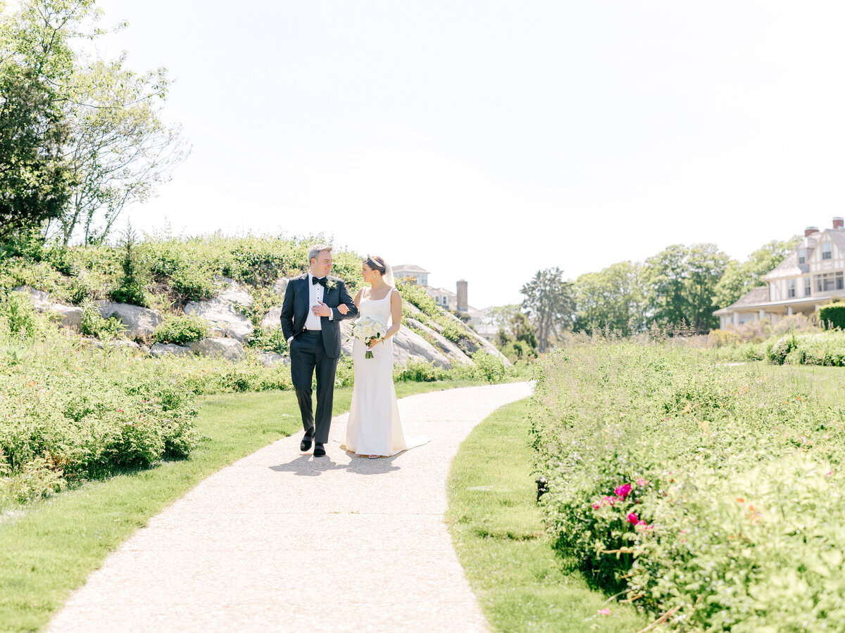 Landscape image of bride and groom walking arm in arm down a path surrounded by grass and bushes
