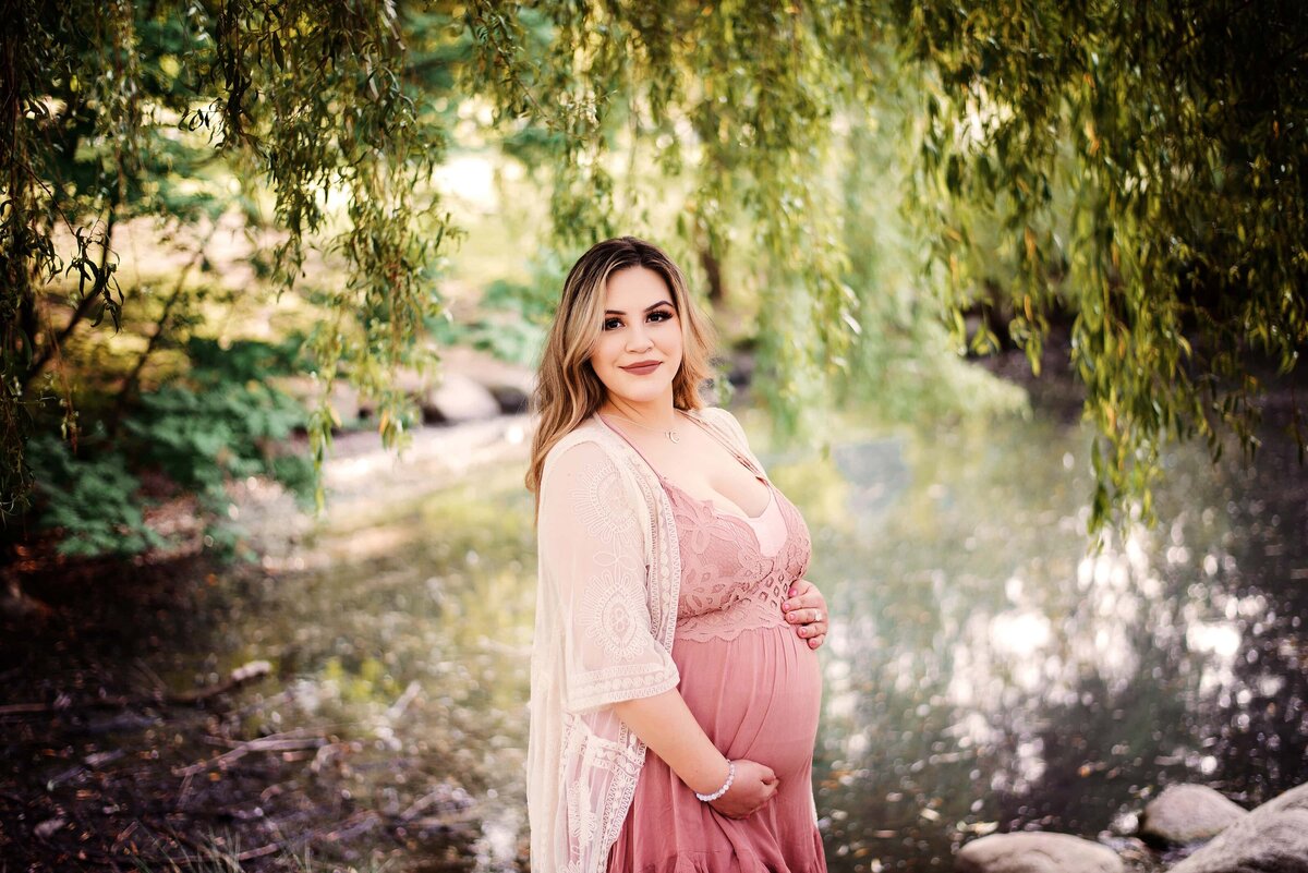 Mother to be in pink and cream boho outfit surrounded by weeping willows.