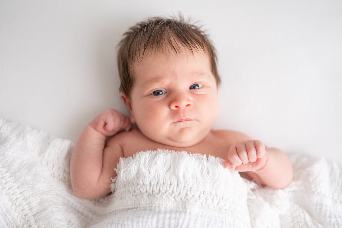 A newborn baby with lots of black hair staring at the camera