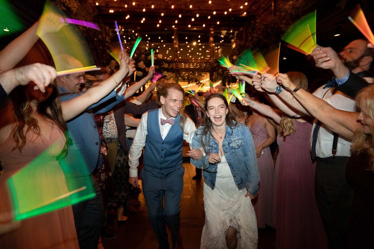 A couple walking through a tunnel of their wedding guests who are holding glow sticks.