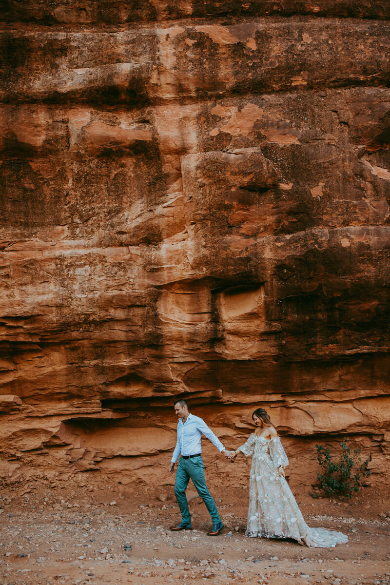 man leads a woman in front of red rocks
