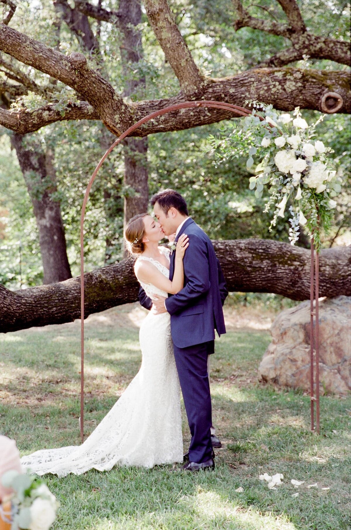 Husband and wife kiss passionately under the woods after a successful farm wedding.