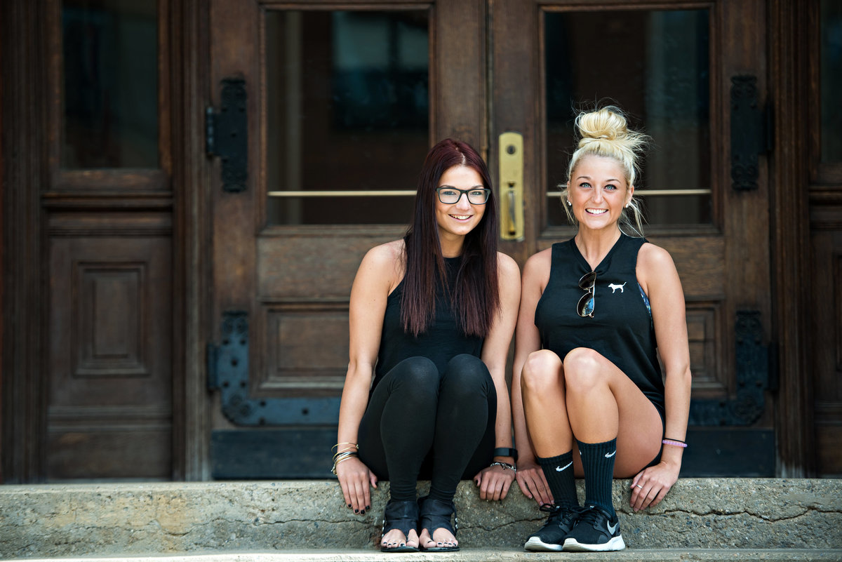 Two college fitness students sit on the steps on campus.
