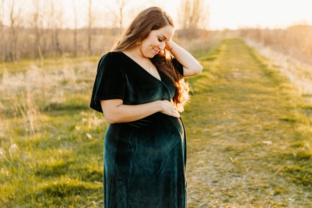 pregnant woman smiling as she glances down at her baby bump and pulls hair behind her ear captured by Green Bay maternity photographer Ashley Kalbus