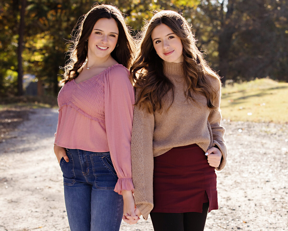 Sisters posing back to back on gravel path surrounded by golden leaves at Anne Springs Close Greenway Charlotte NC