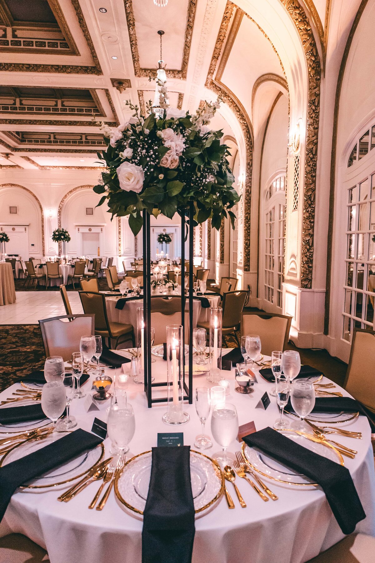 Elegant banquet hall setup, designed by a top wedding planner in Des Moines, with a large floral centerpiece on a table, surrounded by candles, fine china, and gold cutlery. Ornate