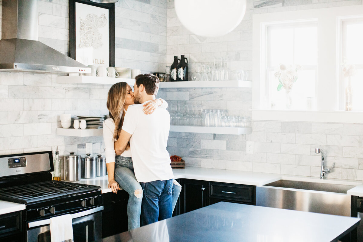 couple sitting on a countertop in a kitchen kissing in home