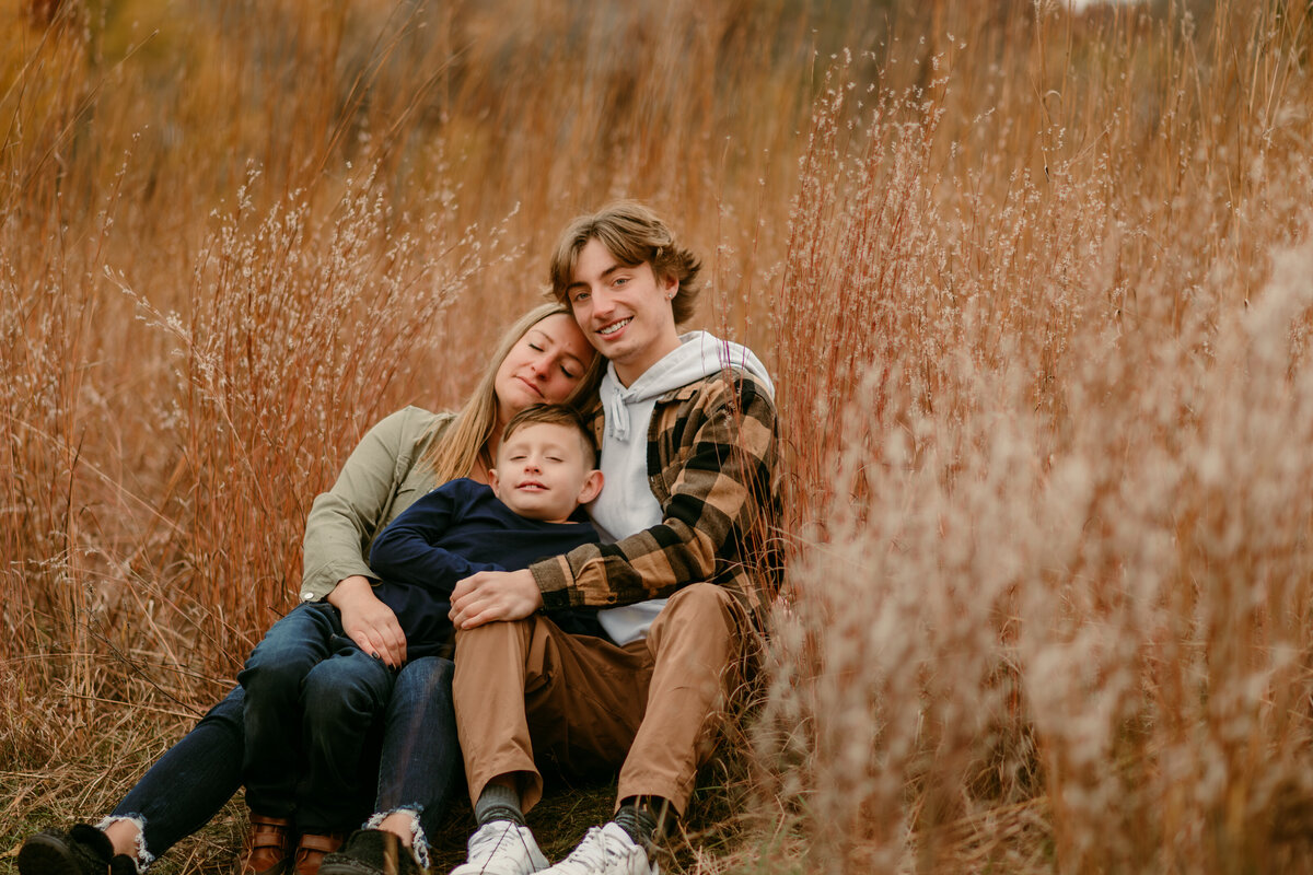 Experience the serenity as a single mom and her two boys share a heartfelt embrace amidst the tranquil beauty of Tamarack Nature Center in White Bear Lake. This touching family moment is captured in a field of tall, dried grass, creating an intimate connection with nature