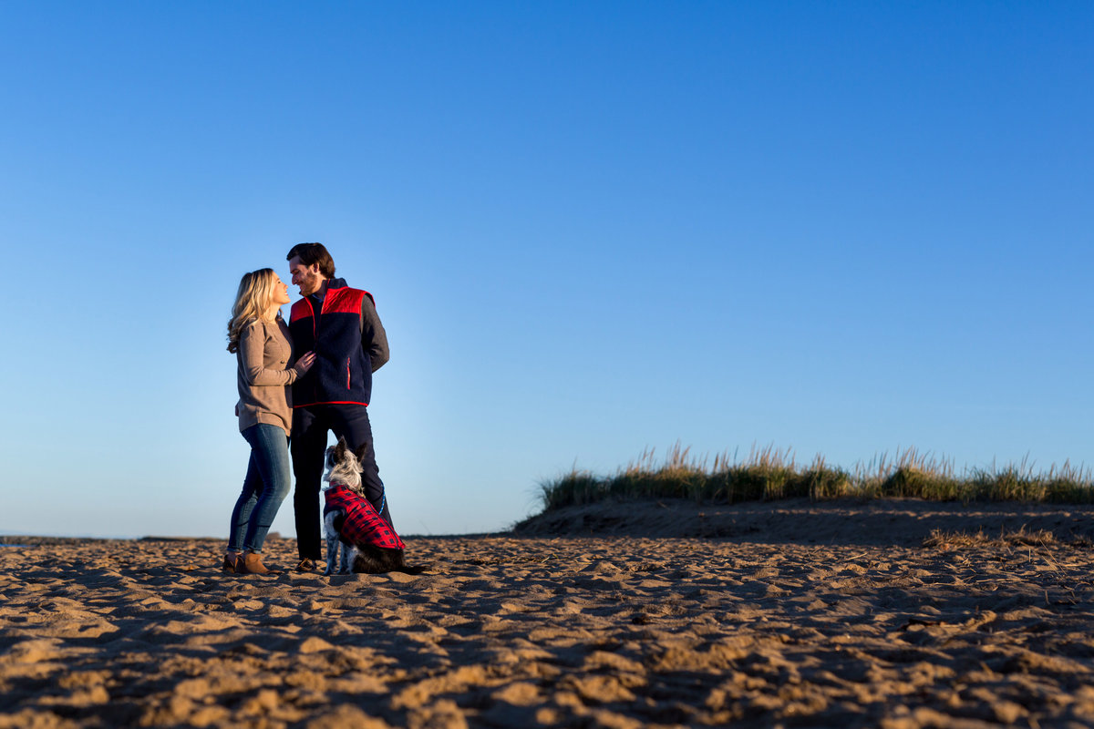 The couple laughs with their dog at the beaches of Plum Island MA