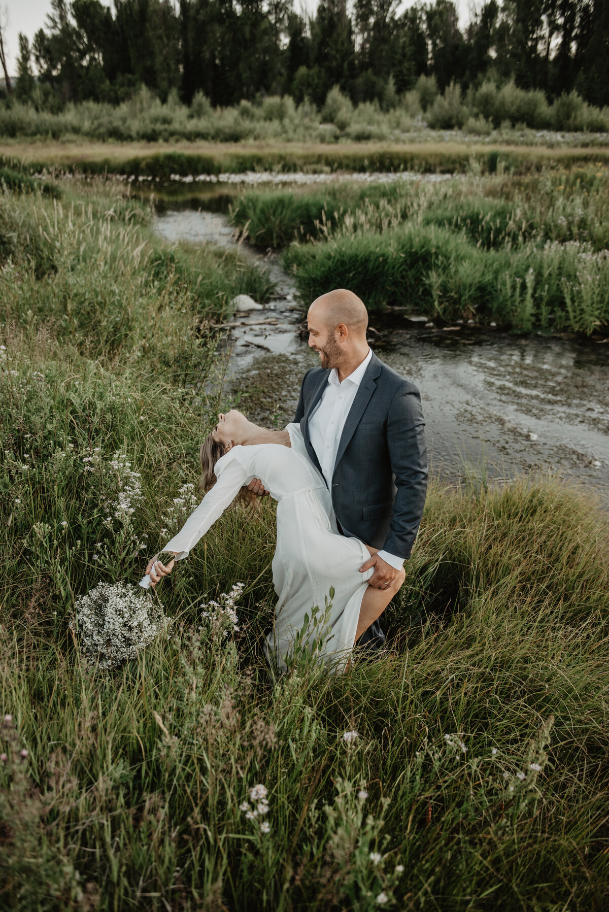 jackson wyoming photographer photographs groom dancing with his bride and dipping her backwards next to snake river for their grand teton wedding