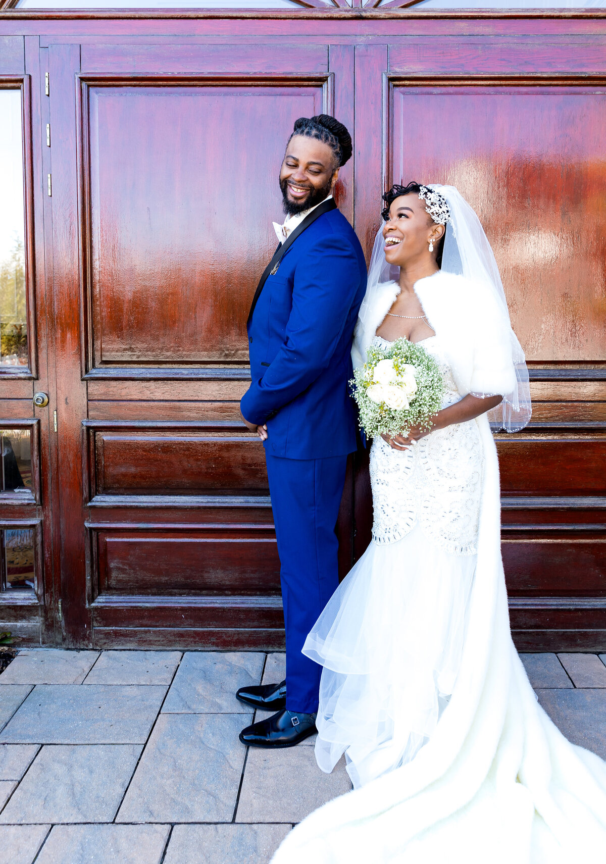 Black bride and groom  standing in front of church door smiling at each together. Their wedding is at the merion catering.