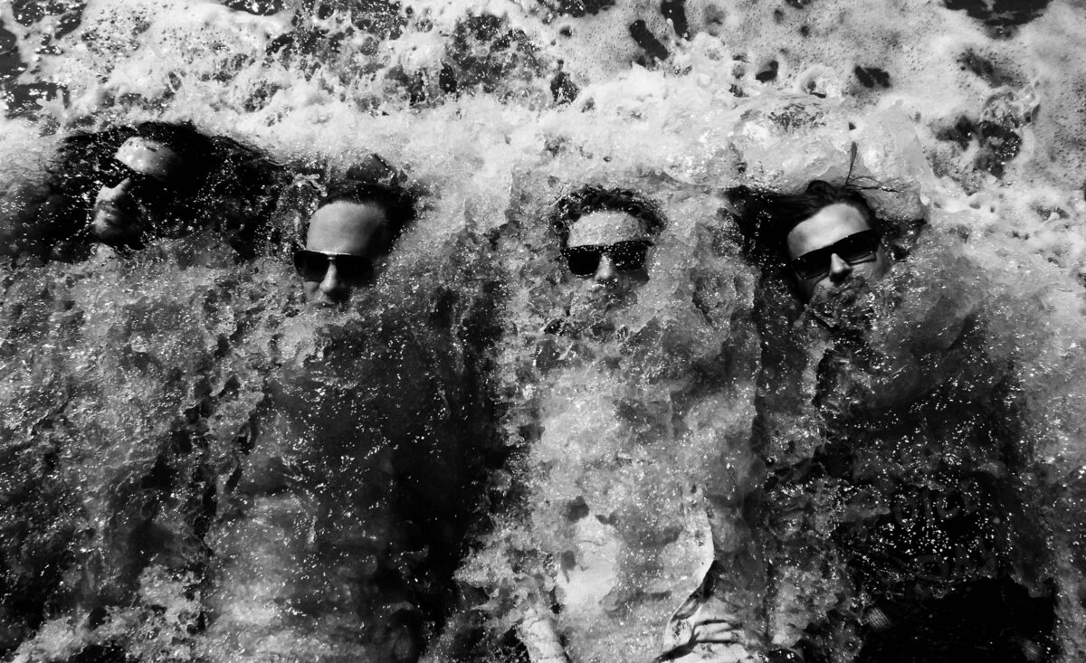 Music group portrait One Bad Son black and white laying on backs with waves crashing over them