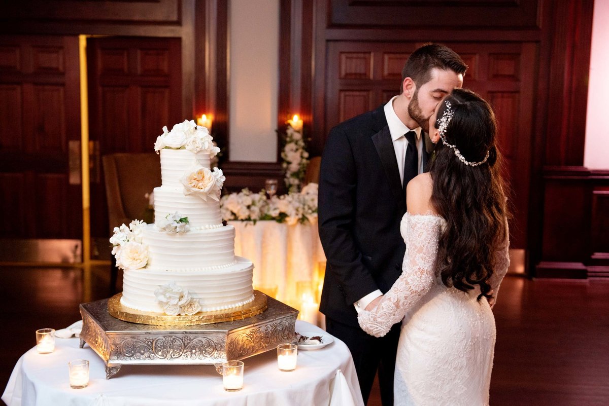 Bride and groom kissing next to their wedding cake at The Mansion at Oyster Bay