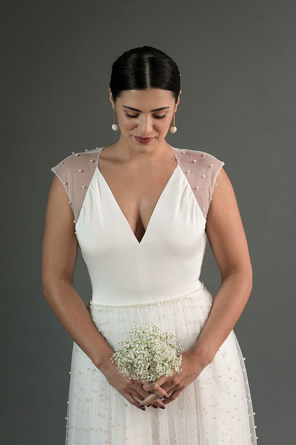 Close-up of the bodice. The v-neck wedding dress features sheer shoulder panels covered in the same pearl tulle as the skirt.