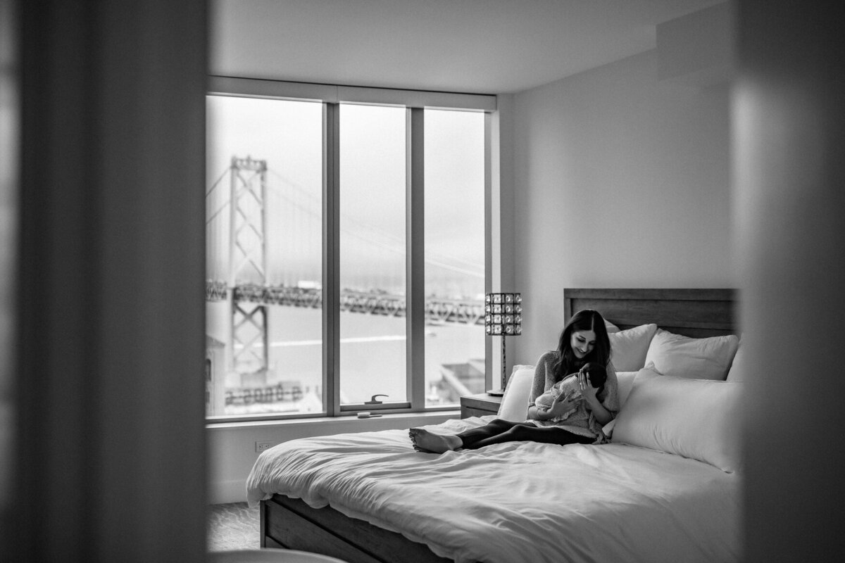 San Francisco bay bridge view from bedroom window with mother holding newborn baby