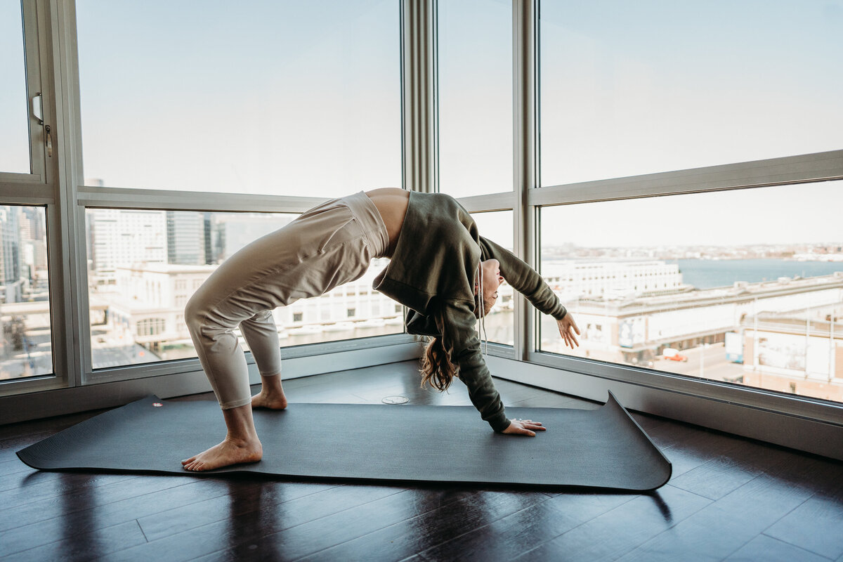 back bend on a yoga mat with city skyline out windows