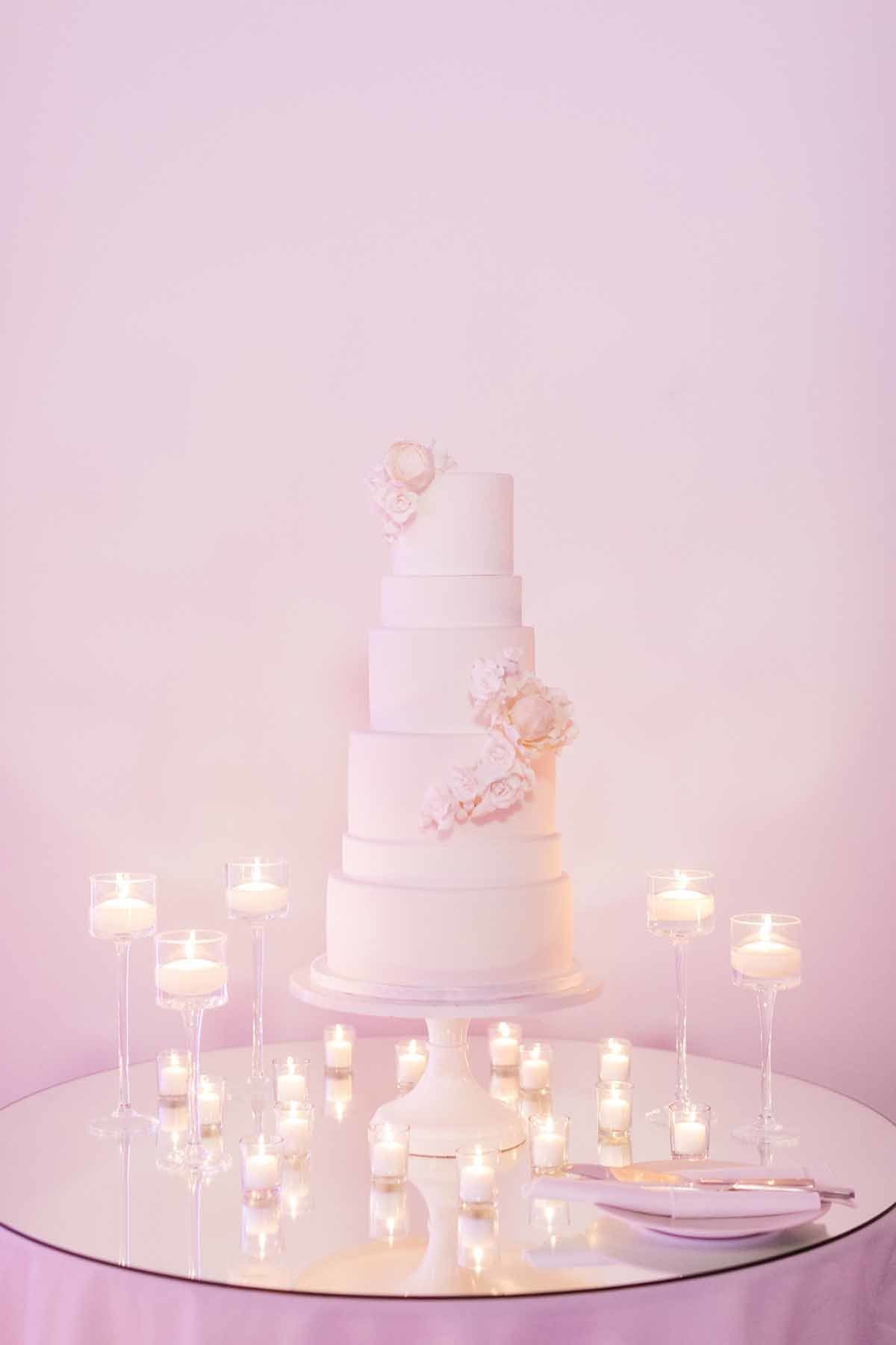 Amazing white tired wedding cake lit by candles on a mirrored table!