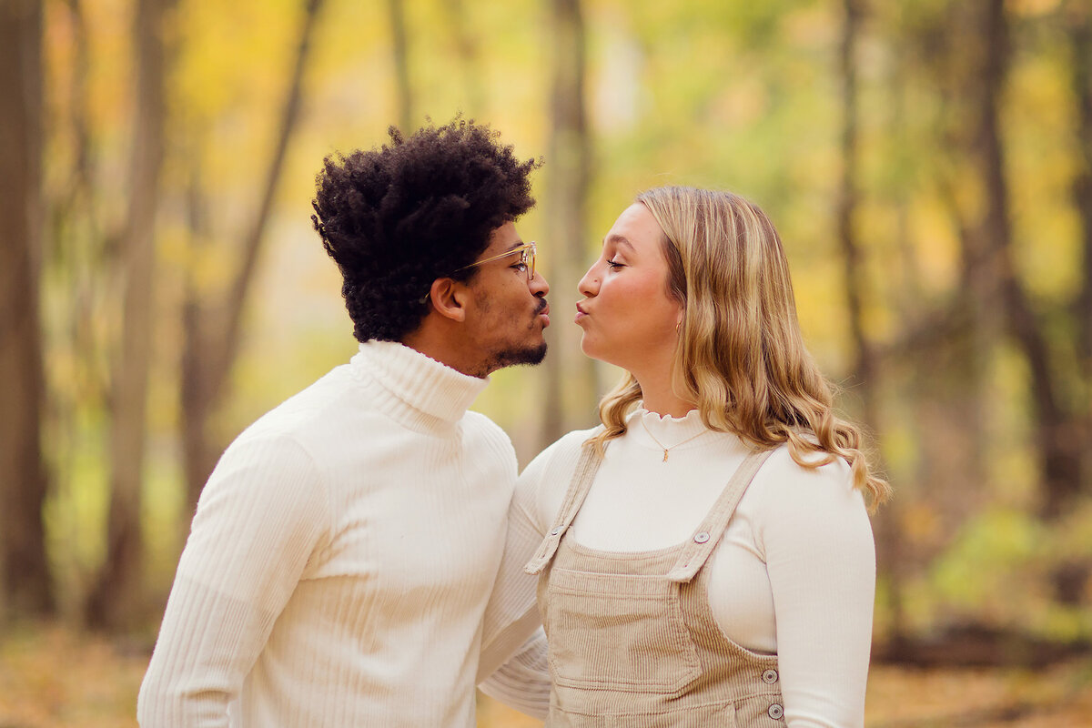Couple almost to a kiss with gorgeous fall colors behind them, both in cream tops.