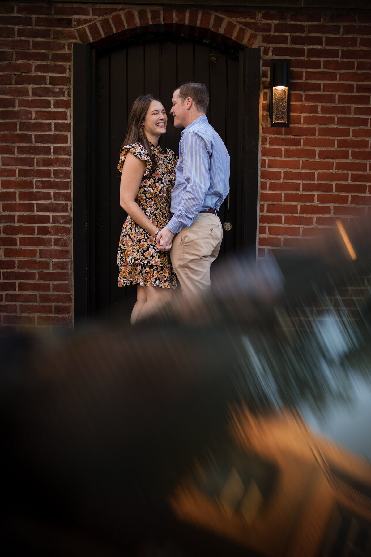A couple holding hands and smiling while standing in front of a red brick building.