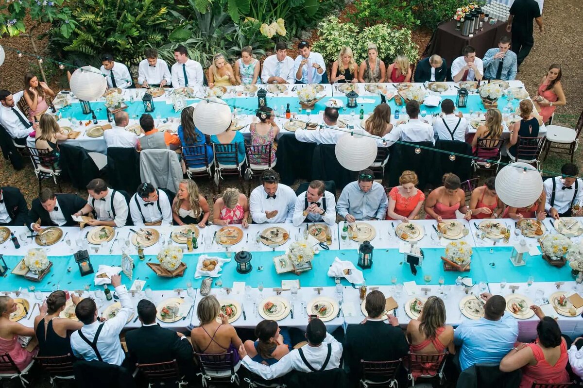 An overhead view of a long dining table at a wedding, with guests seated around in conversation
