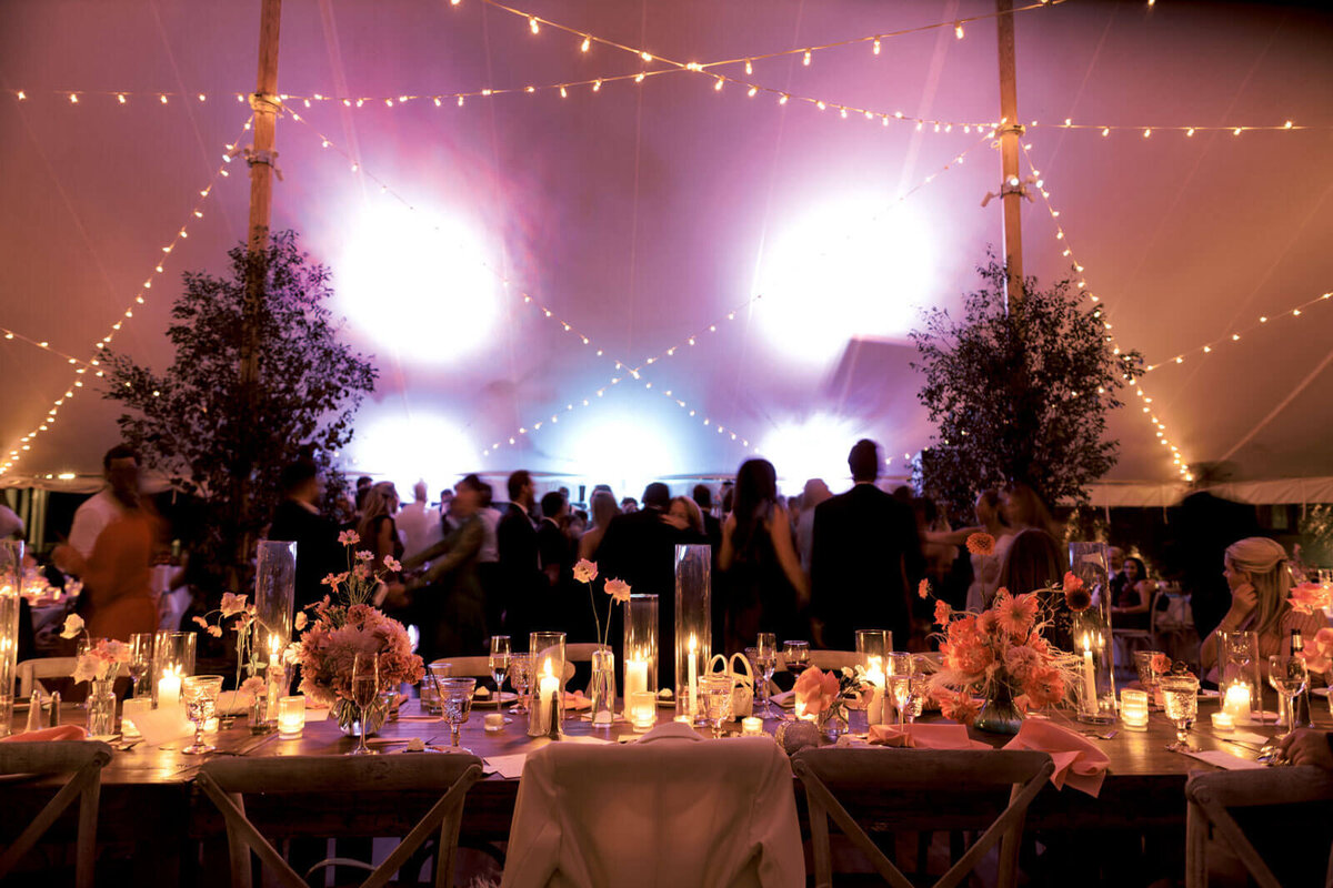 Guests are dancing in an elegant tent wedding reception, adorned with fairy lights and candle-lit tables at The Ausable Club, NY.