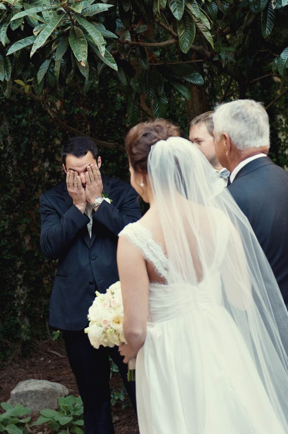 a groom cries and hides his face as his bride comes down the aisle