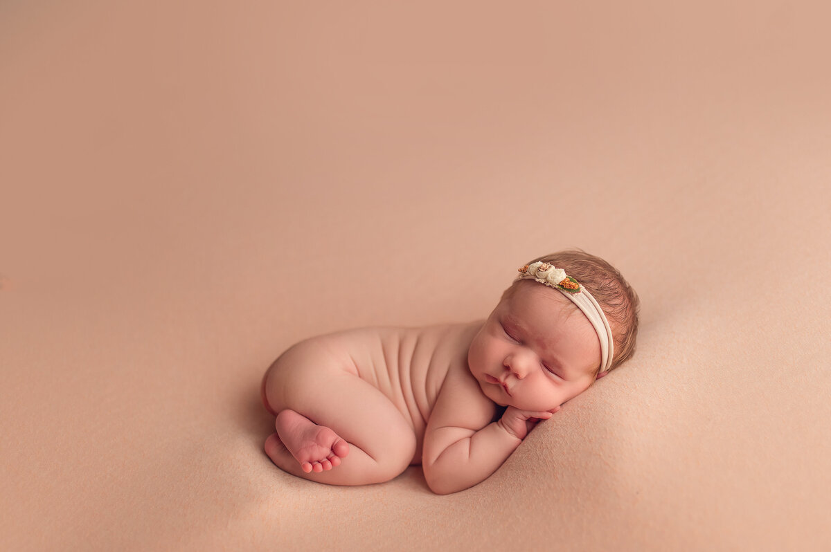 Minimalist newborn portrait with a baby girl sound asleep on a nude-toned background in our Waukesha studio.