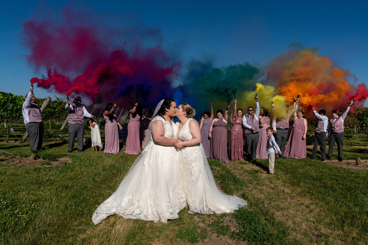 Lesbian couple kiss in front of rainbow smoke bombs.