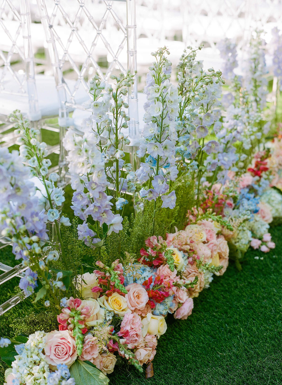 Pink, blue, purple, green, yellow pastel flowers lining wedding aisle at farm ceremony.