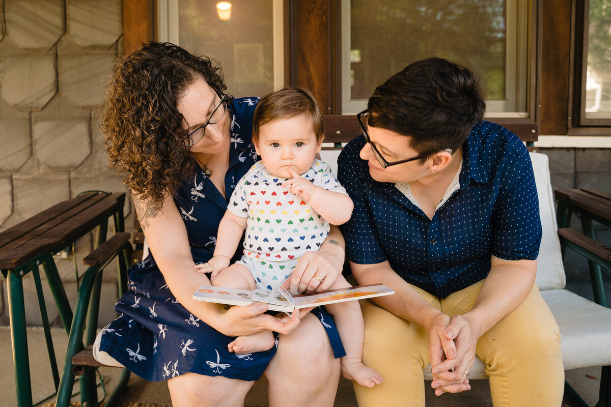 Two parents with a small baby on their lap reading a book together.
