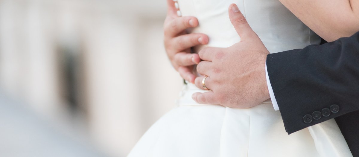 Groom's hands around bride's waist with his wedding ring photo