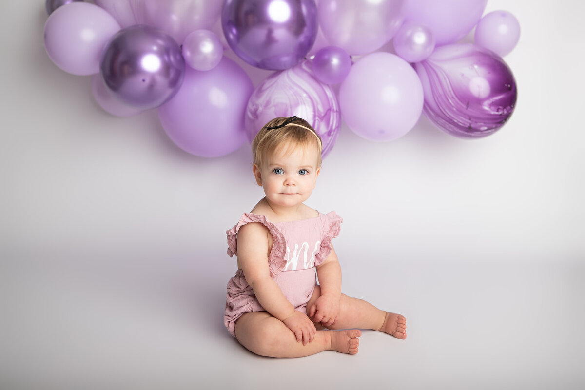 Baby girl eating a messy cake with a purple balloon garland