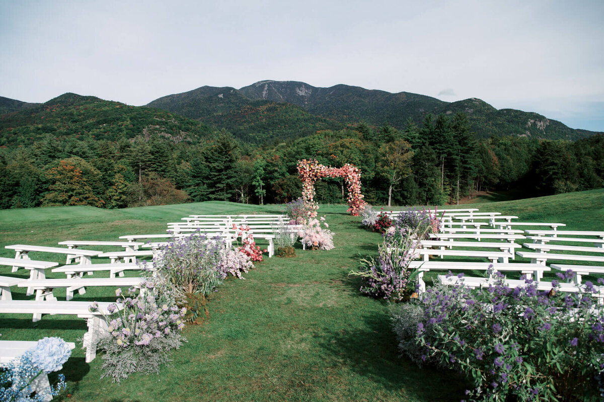 An outdoor wedding ceremony set-up with an arch and aisle full of flowers at The Ausable Club, NY. Image by Jenny Fu Studio.