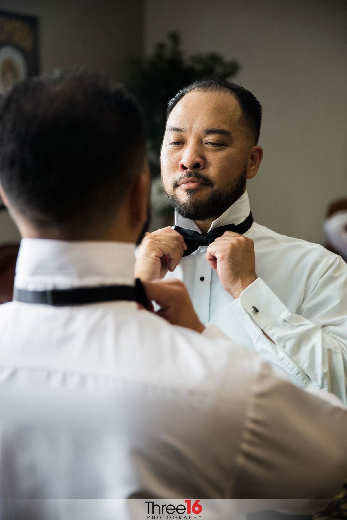Groom straightens his bow tie in the mirror before his wedding