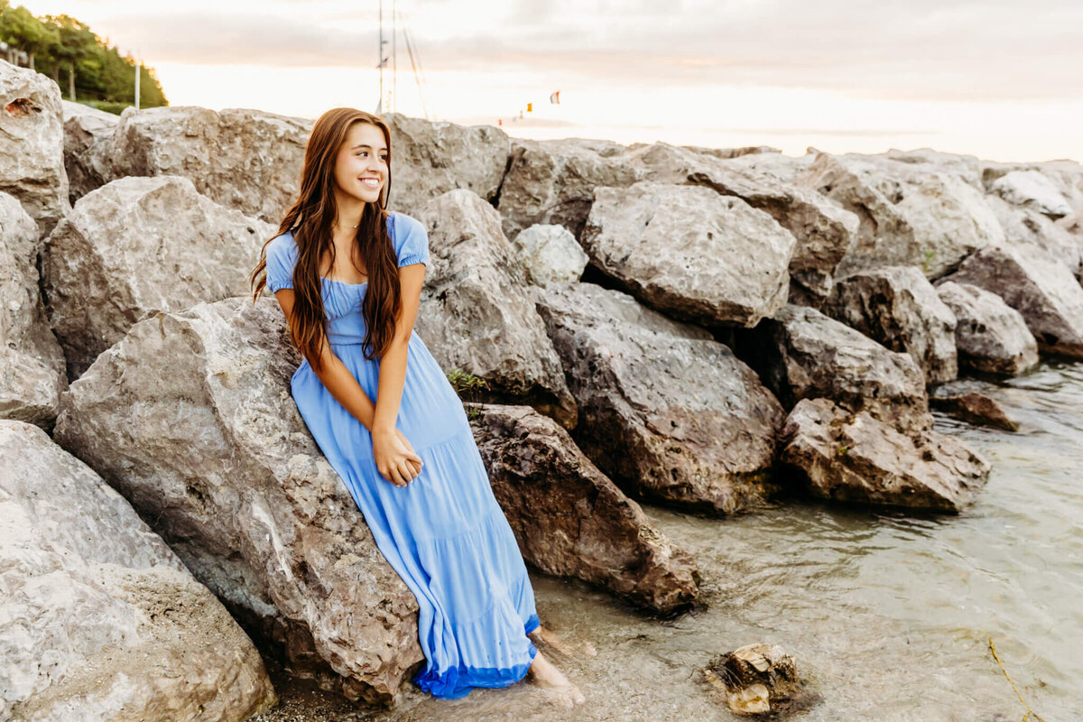 Green Bay senior photographer Ashley Kalbus captures high school girl sitting on rocks at sunset