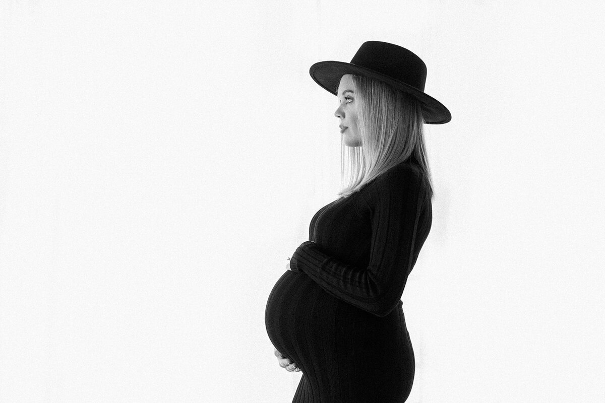edgy black and white maternity photo of woman’s profile in black dress and a large brim hat