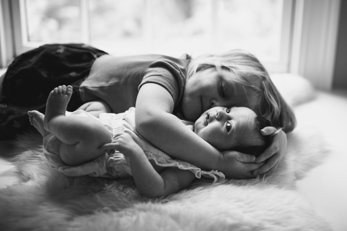 a toddler girl hugs her baby sister