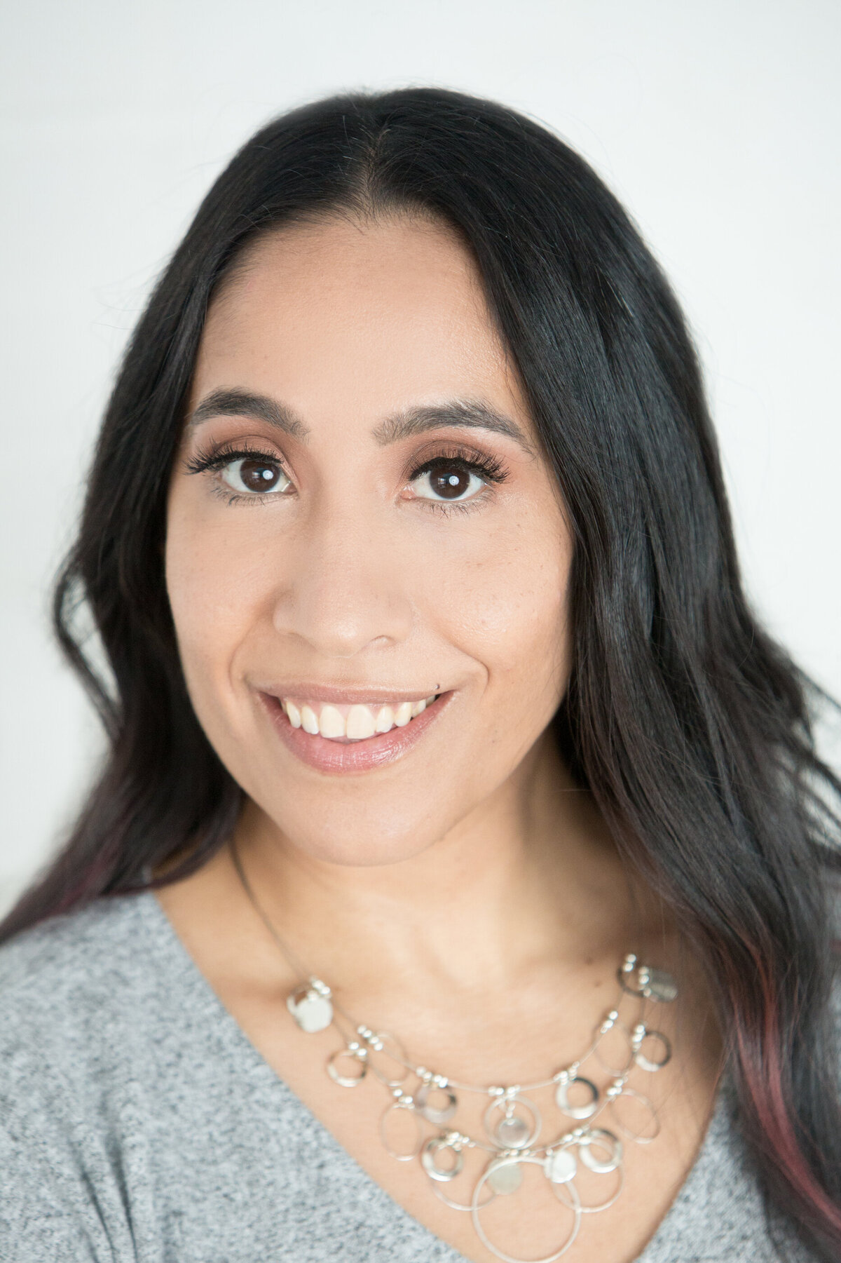 headshot of Latina woman with dark hair and brown eyes in grey shirt and silver necklace New York branding photographer Milestone Images
