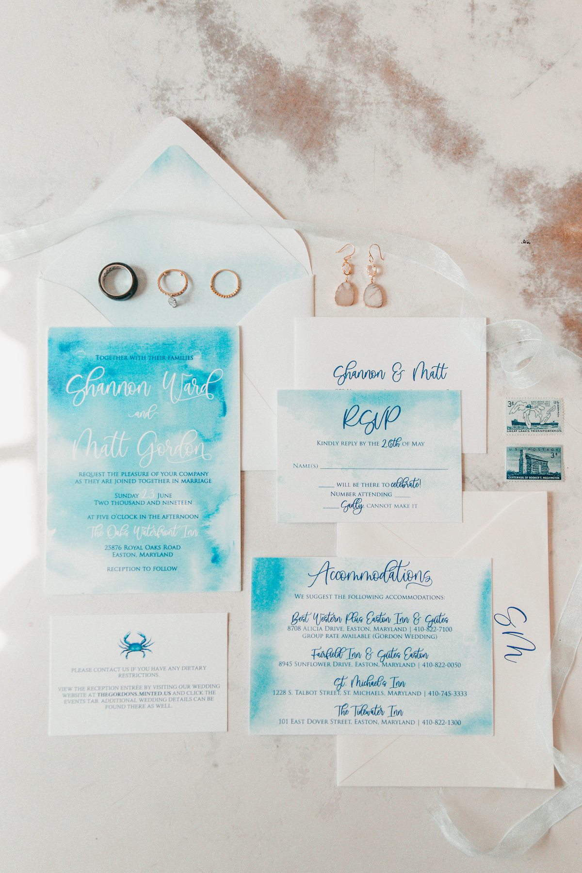 A wedding flatlay of details, including the wedding invitations, rings, and earrings