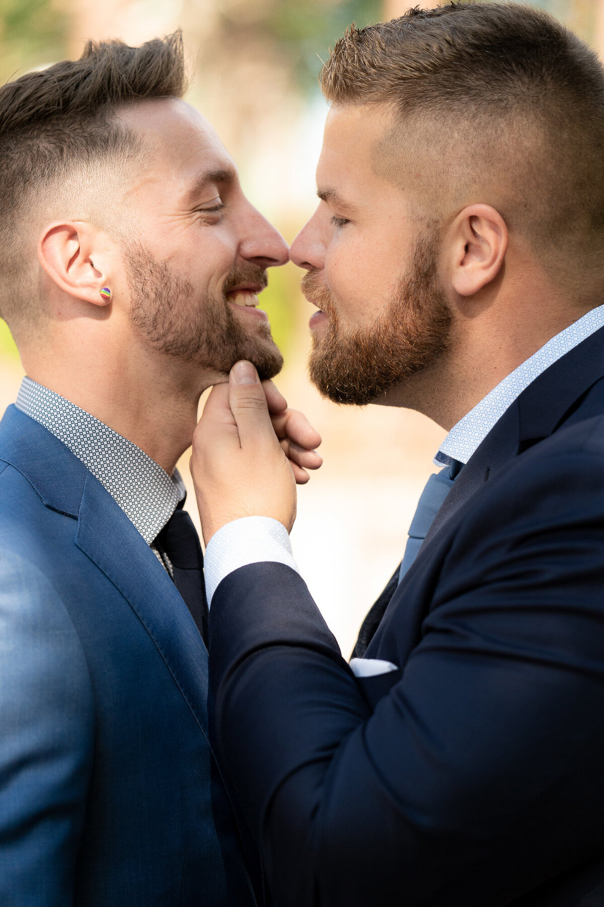 Grooms smile at each other while wearing blue suits.