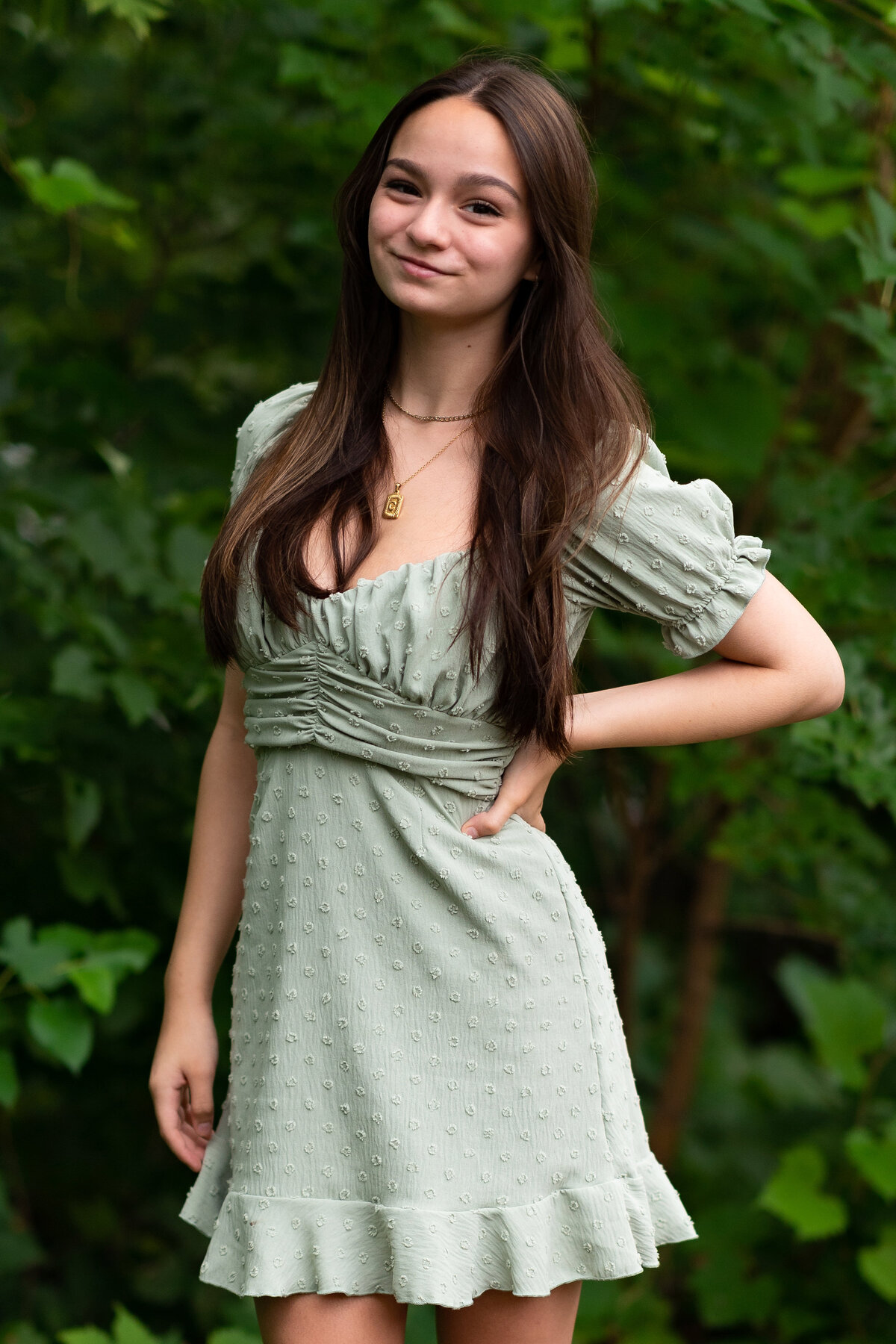 Senior girl dressed in green dress smiles with hand on hip