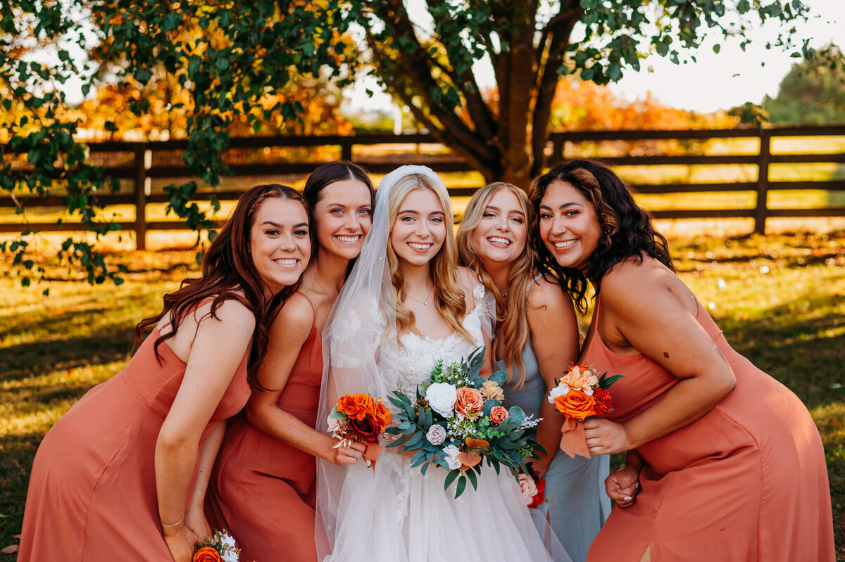 photo of a bride and her bridesmaids smiling in fron t of a wooden fence